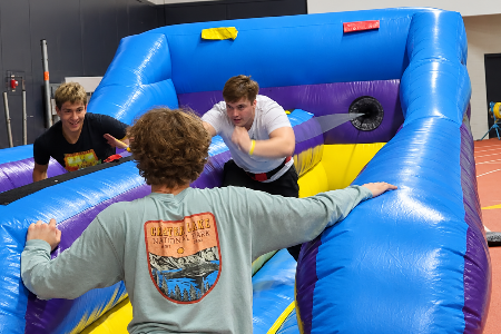 Teens competing on an inflatable bungee run inside a school gym